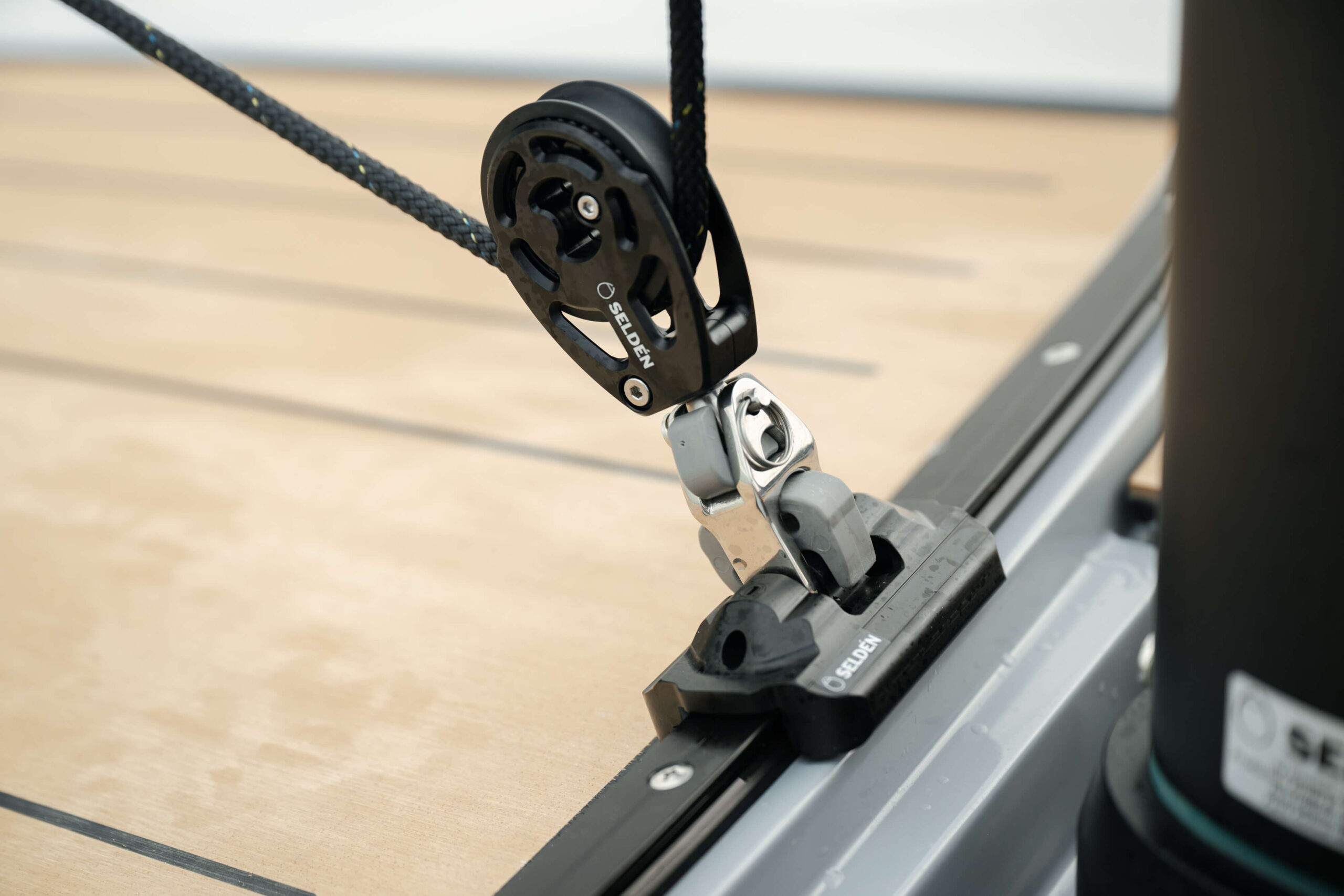 Close-up of a black sailing pulley (Seld&eacute;n) with braided rope threaded through, mounted on a boat's railing track.